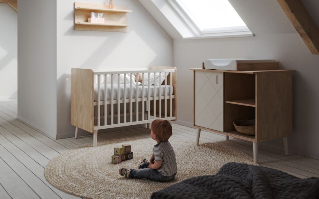 Babaszoba berendezés: kisbaba ül a földön a babaágy és komód előtt.